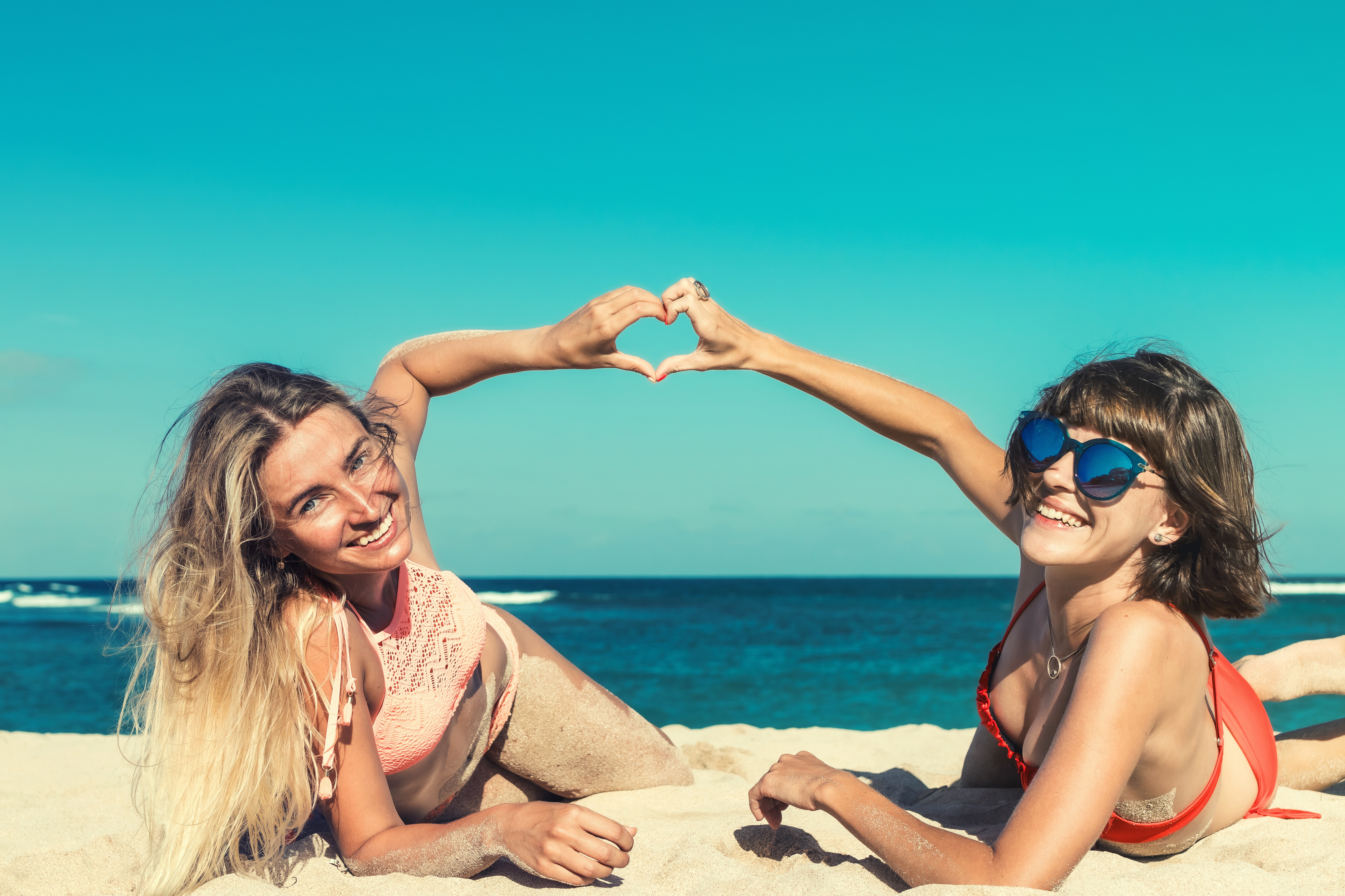 Blije vrouwen op het strand maken hartje met handen